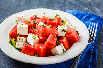 Watermelon salad with feta cheese and herbs in a white plate on blue background.