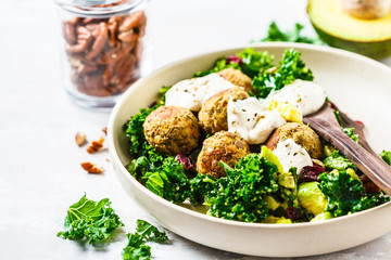Vegan lentils meatballs with green kale salad, avocado and tahini dressing in a white dish.