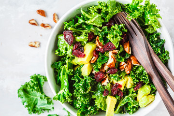 Green kale salad with cranberries and avocado in white bowl, top view. Healthy vegan food concept. - obrazy, fototapety, plakaty