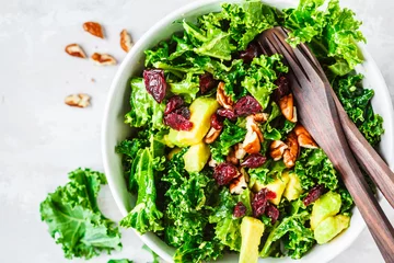 Poster Green kale salad with cranberries and avocado in white bowl, top view. Healthy vegan food concept. © vaaseenaa