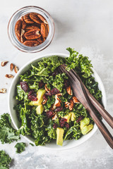 Green kale salad with cranberries and avocado in white bowl, top view. Healthy vegan food concept.