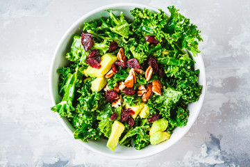 Green kale salad with cranberries and avocado in white bowl, top view. Healthy vegan food concept.