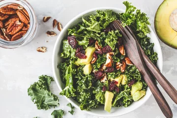 Poster Green kale salad with cranberries and avocado in white bowl, top view. Healthy vegan food concept. © vaaseenaa