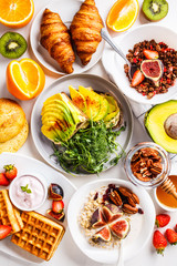 Breakfast table with avocado toast, oatmeal, waffles, croissants on a white background.