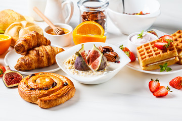 Breakfast table with oatmeal, waffles, croissants and fruits, copy space.