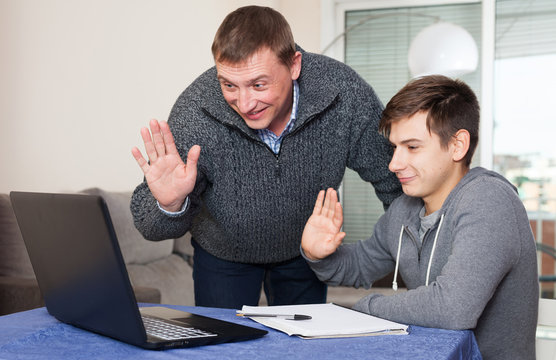 Smiling father with teenager son chatting with relatives online