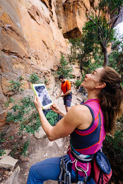 A woman is checks the climbing routes on a cliff in the Blue Mountains while her belayer prepares the rope.