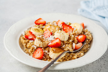 Oatmeal with banana, strawberries and peanut butter in white plate.