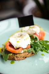 Hot toast with salmon, poached egg, herbs and avocado on a plate with a black copy space flag on a skewer