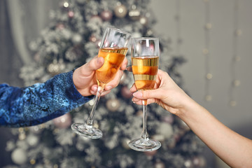 Male and female hands hold glasses with champagne against the background of a decorated New Year tree