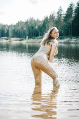 Woman with plus size curvy body in golden futuristic outfit posing in the water