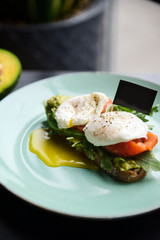 Hot toast with salmon, poached egg, herbs and avocado on a plate with a black copy space flag on a skewer