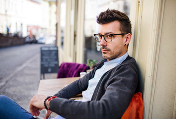 Young sad and serious man sitting in an outdoor cafe.