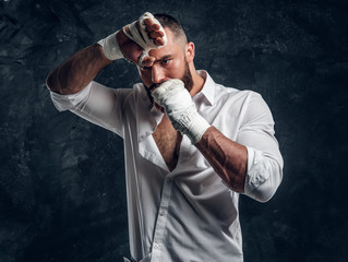 Handsome brutal man in protective boxing gloves is vering mouth guard while posing for photographer.