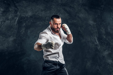Agressive handsome man in white shirt is demonstraiting his punch at dark photo studio.