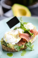 Hot toast with jamon, poached egg, herbs and avocado on a plate with a black copy space flag on a skewer