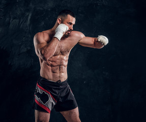 Fototapeta na wymiar Muscular handsome fighter with naked torso is demonstraiting his power at dark photo studio.