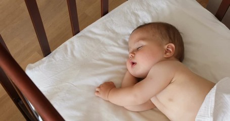 Peaceful adorable baby sleeping on his bed in a room at home. Soft focus. Sleeping baby concept. 1 year-old babyboy sleeps at home, top view