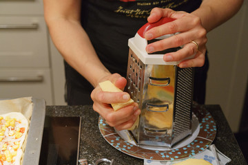 Woman rubs pizza cheese. Photography of pizza preparation process.