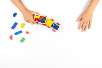 Kid hands playing with toy train and colorful wooden cube blocks on white table background. Top view