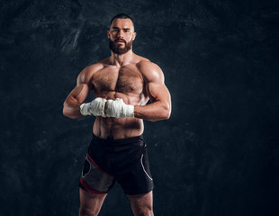 Manly bearded man with beautiful muscular torso is posing for photographer on the dark background.