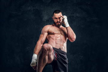Naklejka na ściany i meble Strong muscular fighter is showing his punch while posing for photographer at dark photo studio.