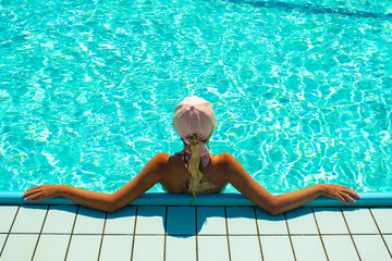 incognito woman back to camera relaxing in swimming pool aquamarine transparent water in summer vacation time, wallpaper background symmetry picture with empty space for copy or text