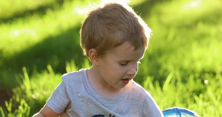 Portrait of little toddler european boy smiling at camera at sunset. Emotionally kid with blue eyes laughing and feel happy. Beautiful portrait of a child boy close-up outdoors in summer time.