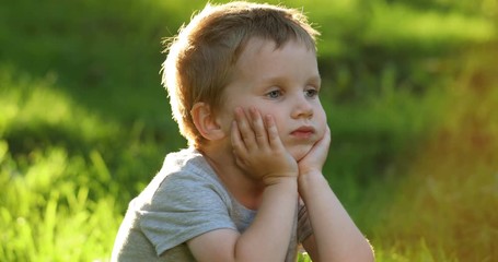 Portrait of little toddler european boy smiling at camera at sunset. Emotionally kid with blue eyes laughing and feel happy. Beautiful portrait of a child boy close-up outdoors in summer time.