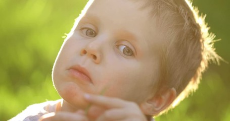 Portrait of little toddler european boy smiling at camera at sunset. Emotionally kid with blue eyes laughing and feel happy. Beautiful portrait of a child boy close-up outdoors in summer time.