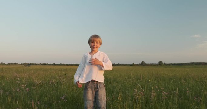 Happy child runs and jumps on green grass on the meadow in the summer. Happy 7 year old cheerful boy is jumping on field. Happiness concept. Active smiling kid on nature in spring. Slow motion
