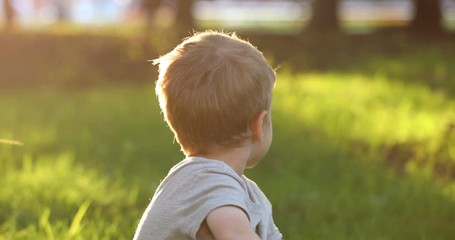 Portrait of little toddler european boy smiling at camera at sunset. Emotionally kid with blue eyes laughing and feel happy. Beautiful portrait of a child boy close-up outdoors in summer time.
