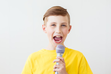Emotional boy sings a song into the microphone with his mouth wide open. Copy space