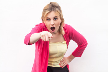 Portrait of shocked beautiful blond young woman in yellow shirt and red blouse standing, looking and pointing at camera with surprised face. indoor studio shot, isolated on white wall background.