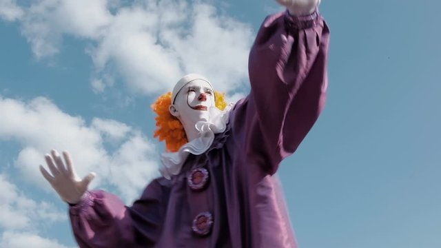 Dancing clown in the image of a pennywise. A guy with makeup and in a suit similar to IT is dancing against the sky with clouds. Cosplay or Halloween celebration.