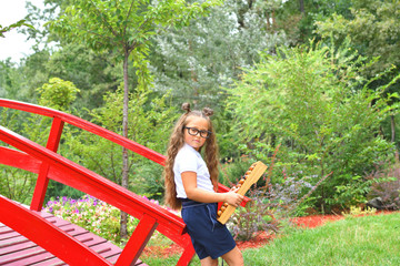 Naklejka na ściany i meble Portrait of beautiful young first-grader girl with large abacus. Thoughtful schoolgirl using a maths abacus . calculation.background park and red bridge