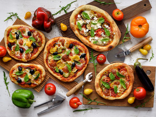 Vegetarian pizza set. Flat lay of homemade big and small pizzas with olives, eggplants, bell peppers, tomatoes and basil served with raw vegetables on white background