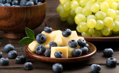 .cheese with blueberries and grapes on a wooden background