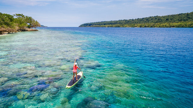 A woman paddling a stand up paddleboard over a coral  reef off the coast of Espiritu Santo, Vanuatu.