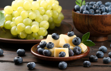 .cheese with blueberries and grapes on a wooden background