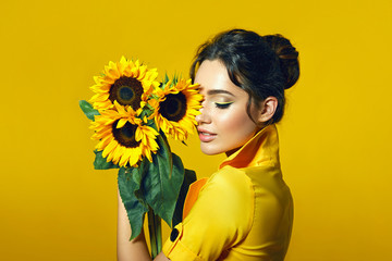 A girl in a yellow dress holds in her hands a bouquet of yellow sunflowers.