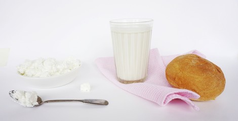 a plate with cottage cheese, a spoon with cottage cheese, a glass of milk, a bun on a white background, healthy natural food