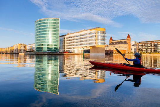 A woman is paddling a sea kayak early in the morning past Midtermolen, a pier in the Southern Free Port of Copenhagen, Denmark.