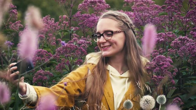 Pretty woman taking selfies on a smartphone. Young girl in glasses among flowers