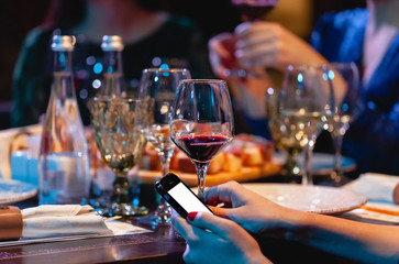Woman holding a glass of red wine and phone. Dinner at the restaurant, party