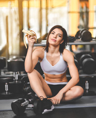 Young sporty woman has a break in training in the gym. makes a snack banana.