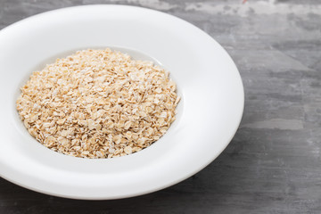 uncooked oats in white plate on ceramic background