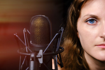 Brunette girl for a professional microphone, close-up. Professional record of the singer in the Studio. Female vocalist on black background in recording Studio.