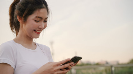 Cheerful Asian tourist blogger woman using touchscreen technology at smartphone while walking on the street at downtown city in the evening. Lifestyle backpack tourist travel holiday concept.