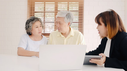 Asia smart female agent offers health insurance for elderly couples by document, tablet and laptop. Aged Asian couple consulting with insurance agent while sitting together with at home.